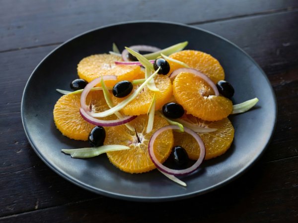 Siciliansk appelsinsalat med hvit fennikel, svarte oliven og rødløk på en mørk tallerken