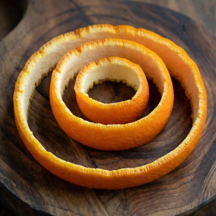 En lang spiral av fersk appelsinskall på et mørkt trebrett